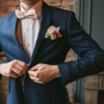 Man buttoning navy suit jacket with boutonniere