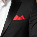 A man in a tuxedo standing in front of a brick wall. In his suit's breast pocket is a bright red pocket square.