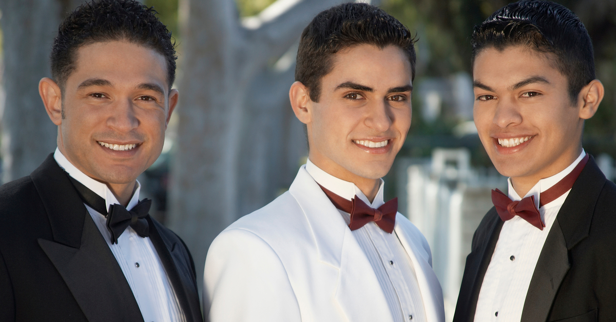 Three young men in suits attending a quinceañera. Two of them are wearing black jackets with a white shirts.
