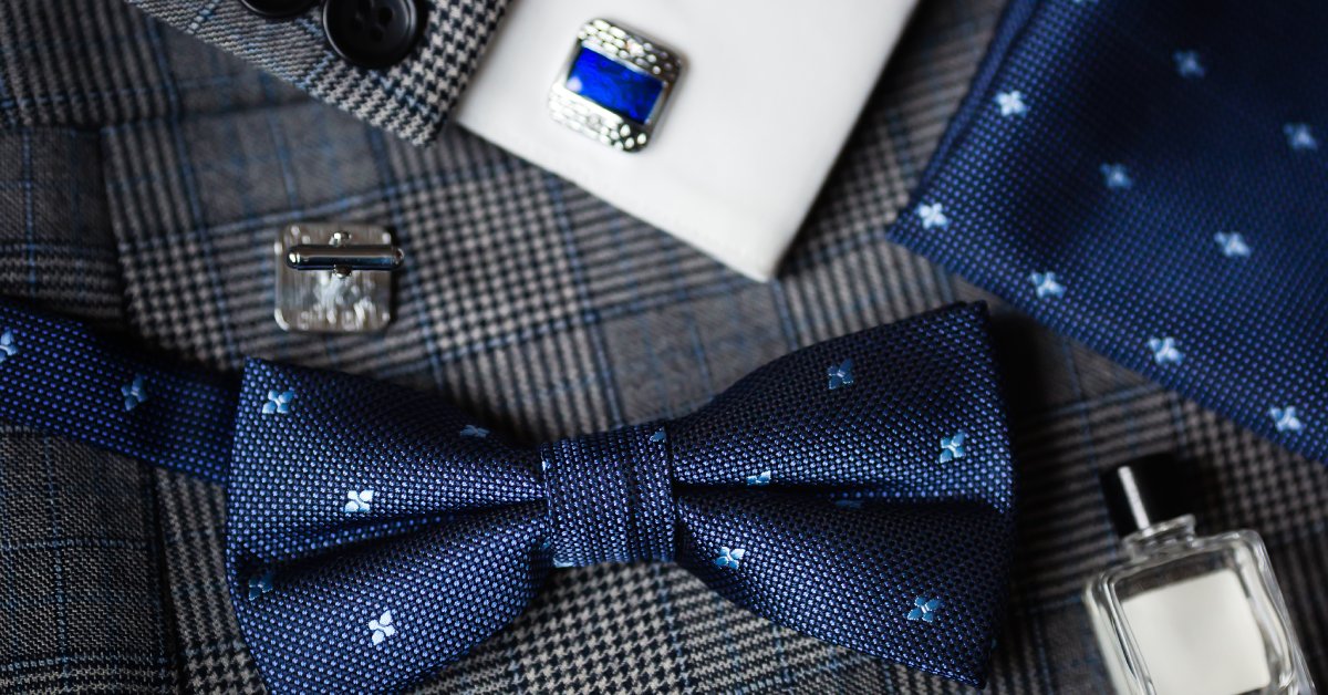 A luxury bow tie, cuff link, and cologne bottle sitting on a vintage suit, ready for a formal event or wedding.