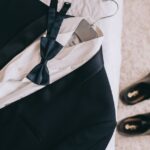 A tuxedo accessories set, including shoes, cuff links, a belt, a watch, and a bow tie neatly arranged on a surface.