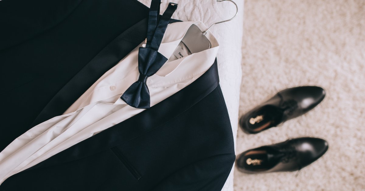 A tuxedo accessories set, including shoes, cuff links, a belt, a watch, and a bow tie neatly arranged on a surface.